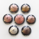 Size comparison between the e.l.f. Studio Baked Eyeshadow and Baked Blush. Starting with the top left and working clockwise: Enchanted, Bronzed Beauty, Toasted, Bark, Moonlight Serenade, and Pixie around the blush Peachy Cheeky.
